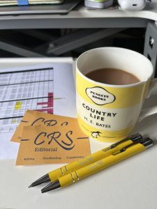 CRS Editorial business cards and pens, with a cup of tea and papers on a white table.